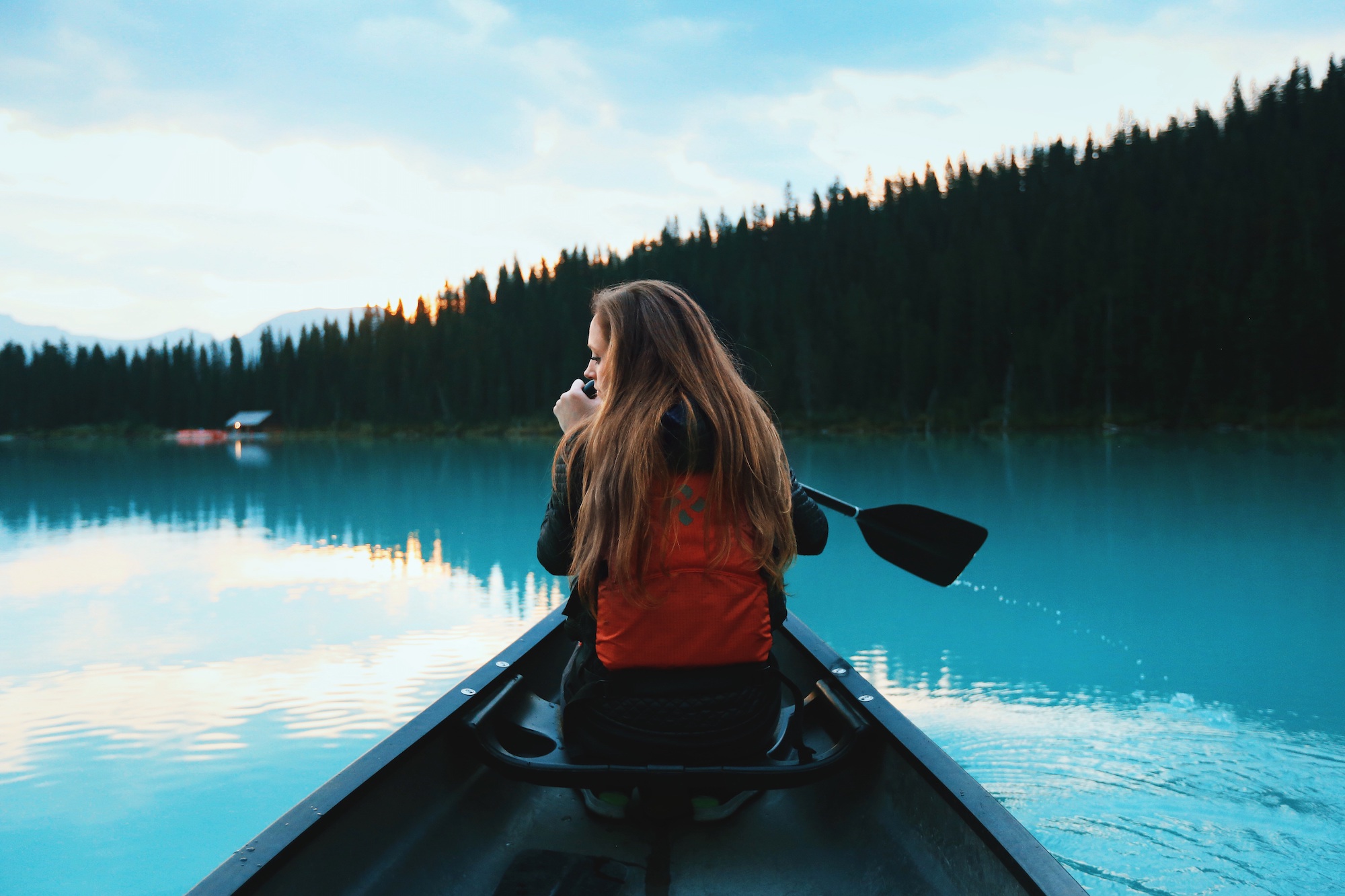 Woman in life vest paddling in a canoe on a blue watered lake.